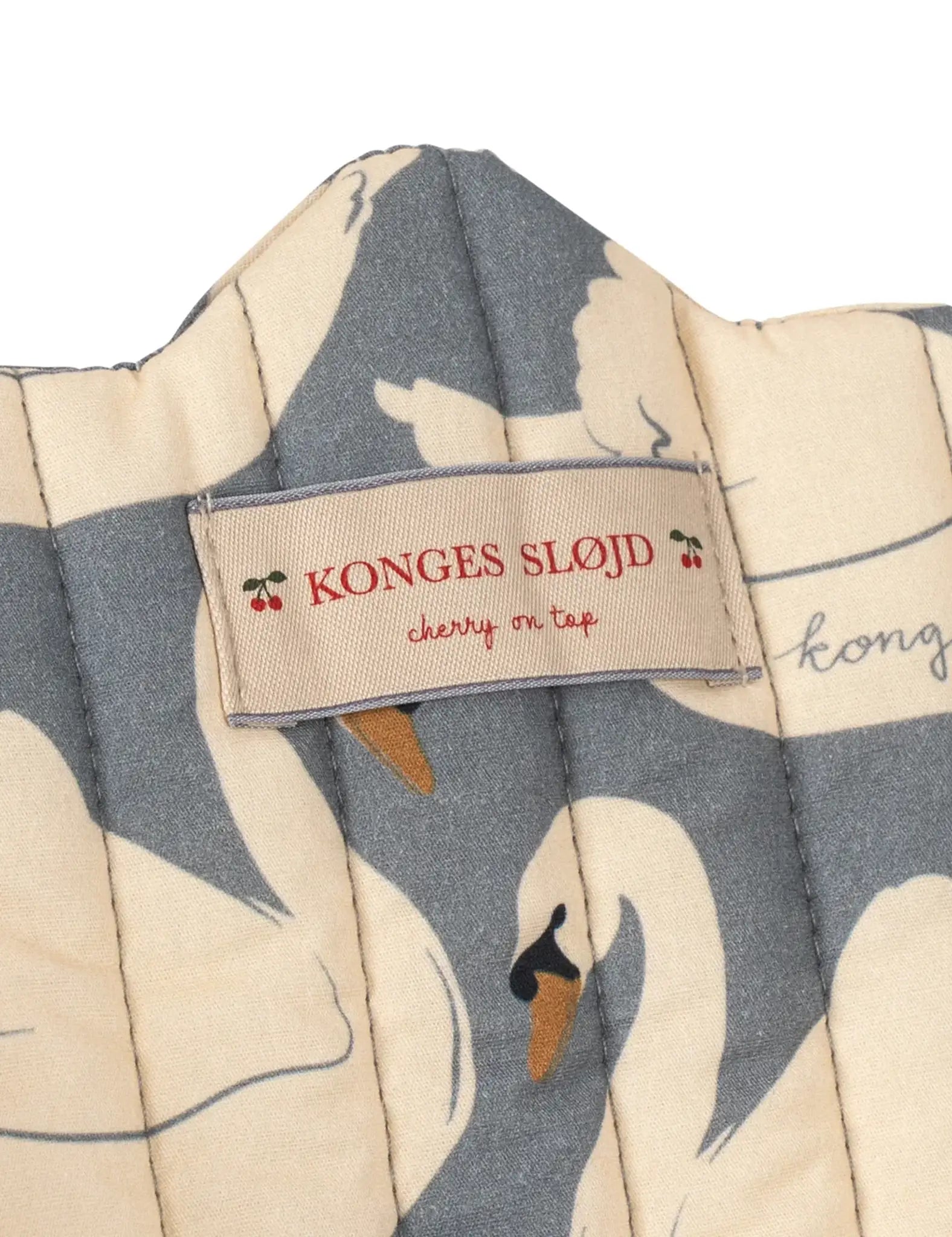 Carrinho para boneca Konges Sløjd com tecido acolchoado estampado de cisnes e etiqueta.