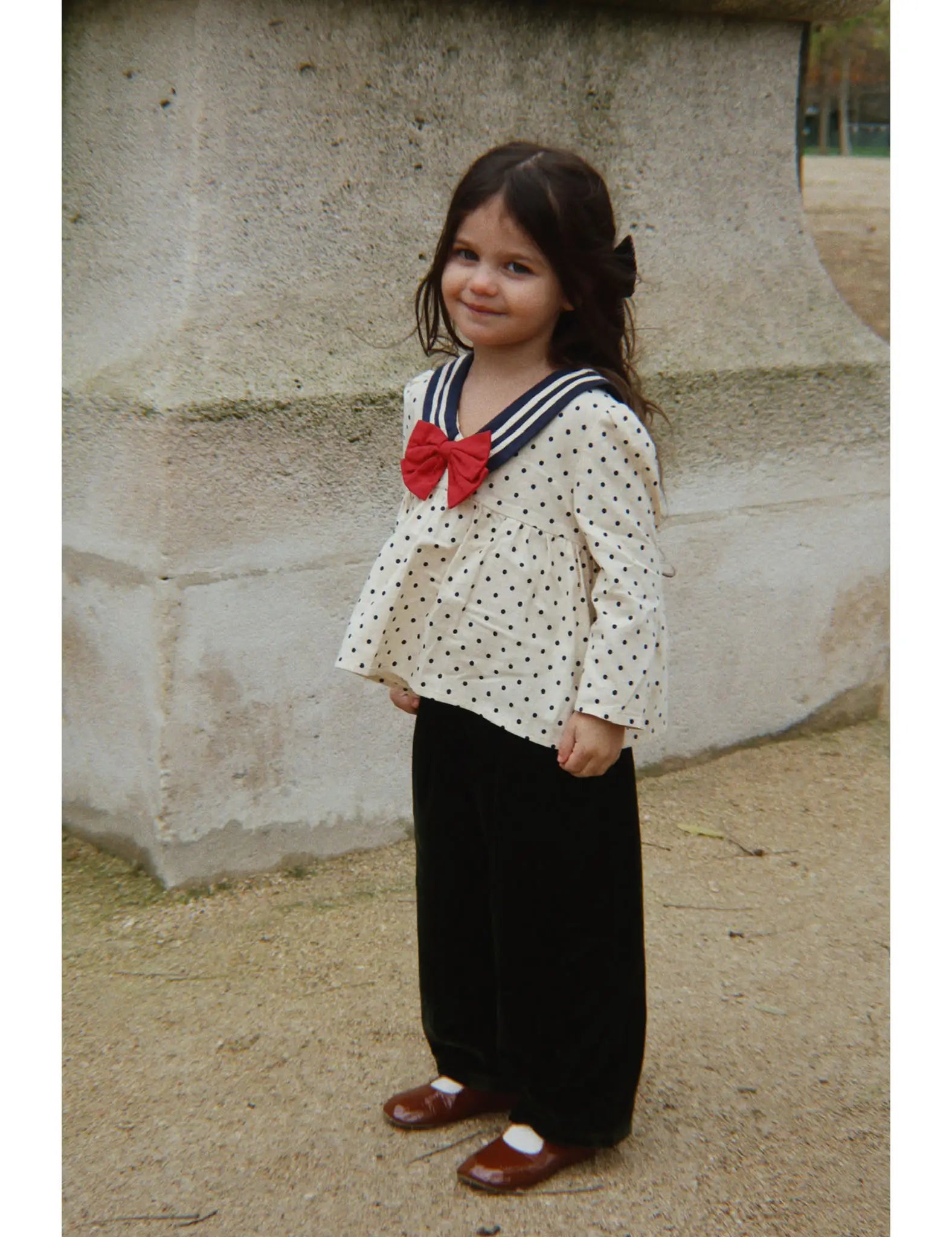 Camisa infantil creme com bolinhas pretas, gola em riscas azul-marinho e laço. Konges Sløjd